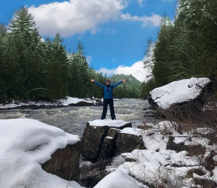 Maude, bras levés sur une roche au milieu d'une rivière enneigée